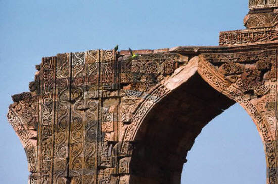 Islamic script and arabesques decorate the ruins of an ogee arch at Qutb mosque